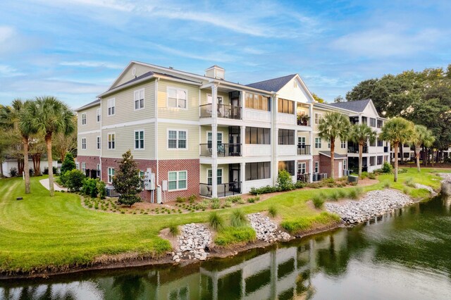 back of house with a balcony, a water view, and a lawn