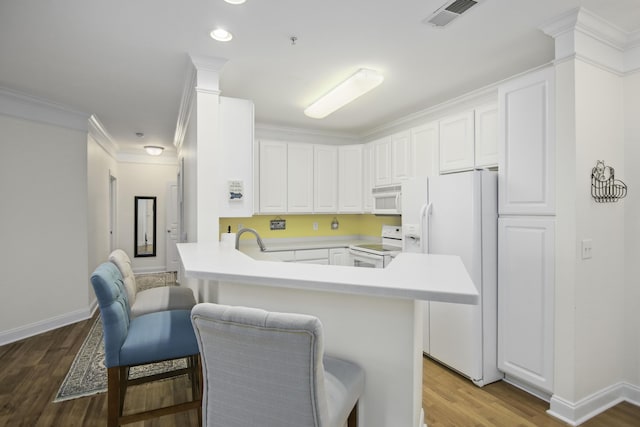 kitchen with white appliances, visible vents, wood finished floors, a peninsula, and white cabinetry