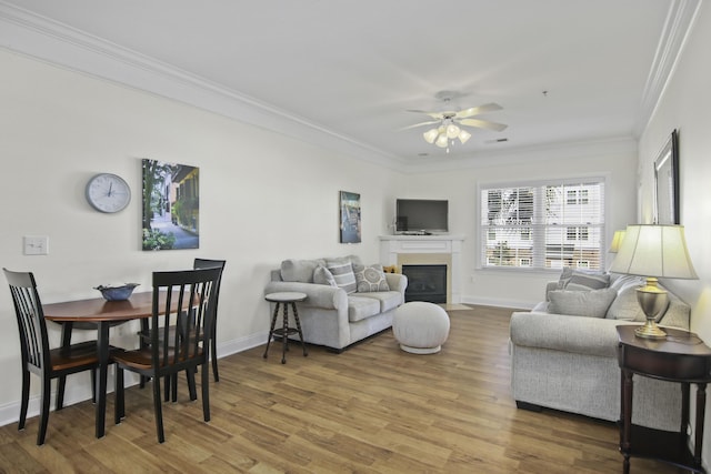 living room featuring a fireplace with flush hearth, wood finished floors, a ceiling fan, baseboards, and ornamental molding