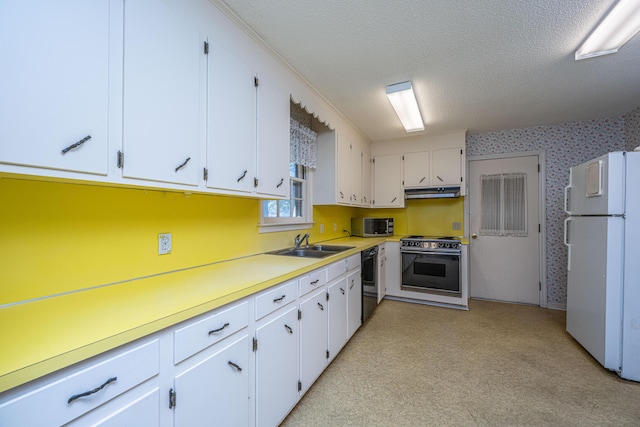 kitchen featuring light countertops, stove, freestanding refrigerator, white cabinets, and wallpapered walls