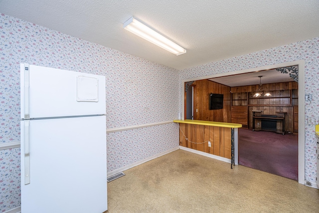 kitchen with wallpapered walls, visible vents, decorative light fixtures, freestanding refrigerator, and a textured ceiling