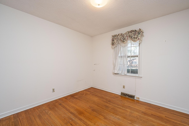 unfurnished room with a textured ceiling, wood finished floors, visible vents, and baseboards