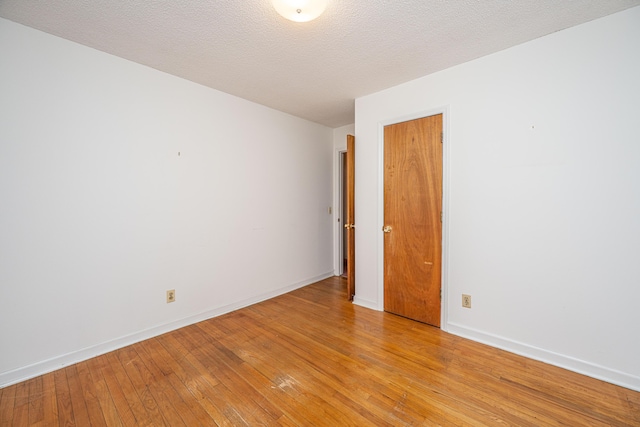 spare room with light wood-style flooring, baseboards, and a textured ceiling