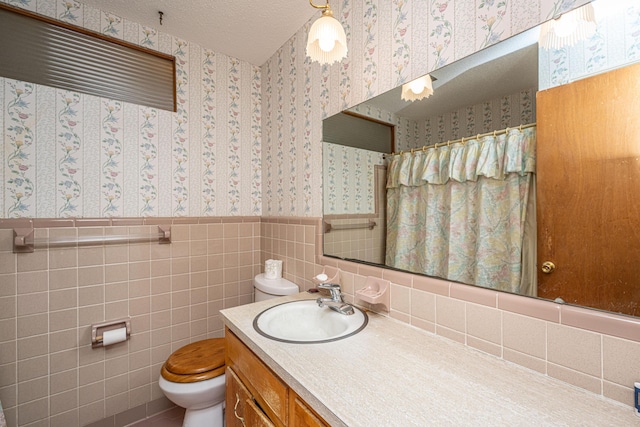 bathroom featuring toilet, wainscoting, a textured ceiling, vanity, and wallpapered walls