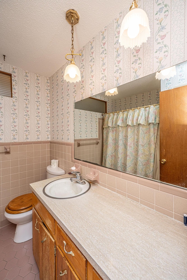 bathroom featuring toilet, wallpapered walls, a textured ceiling, and wainscoting