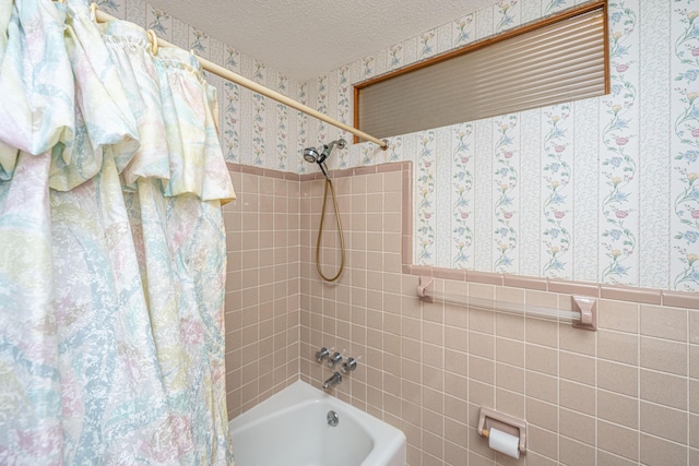 bathroom with a wainscoted wall, tile walls, shower / tub combo, a textured ceiling, and wallpapered walls