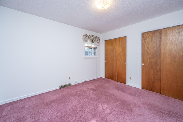 unfurnished bedroom with carpet, multiple closets, visible vents, a textured ceiling, and baseboards