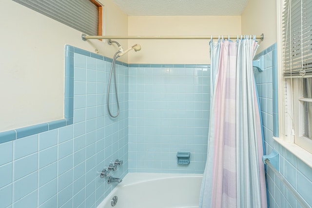 bathroom with a textured ceiling, tile walls, and shower / bathtub combination with curtain