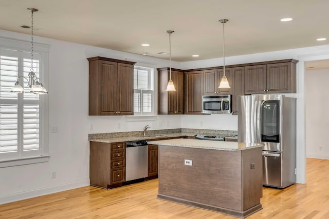 kitchen with light wood-style flooring, a sink, stainless steel appliances, dark brown cabinetry, and a center island