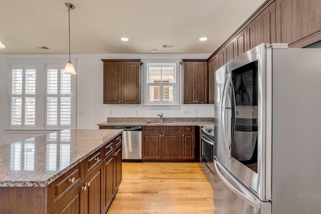 kitchen featuring light stone counters, a sink, light wood-style floors, appliances with stainless steel finishes, and decorative light fixtures