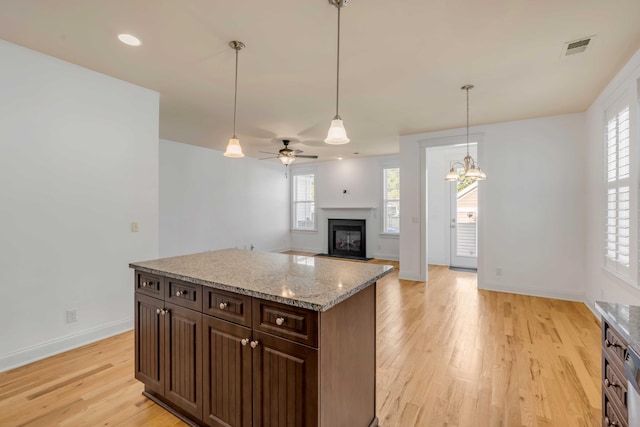 kitchen with a wealth of natural light, visible vents, light wood-style floors, and a glass covered fireplace