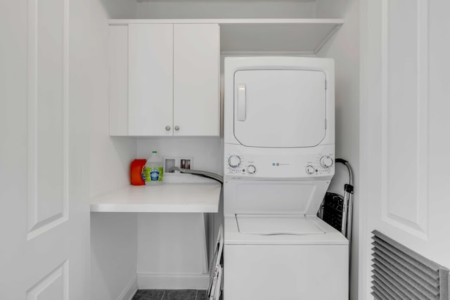 clothes washing area featuring cabinet space, stacked washing maching and dryer, and baseboards