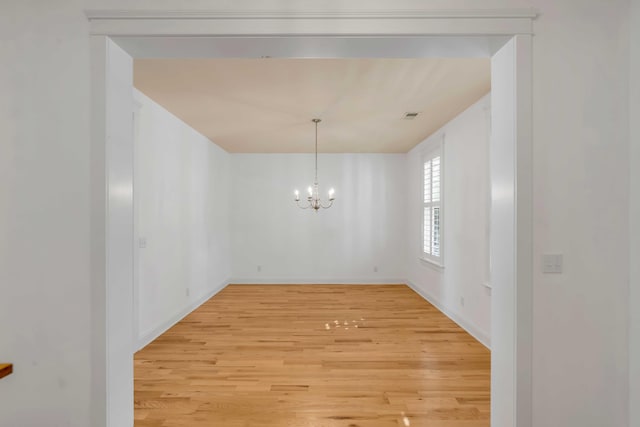 unfurnished dining area with visible vents, baseboards, an inviting chandelier, and light wood-style flooring