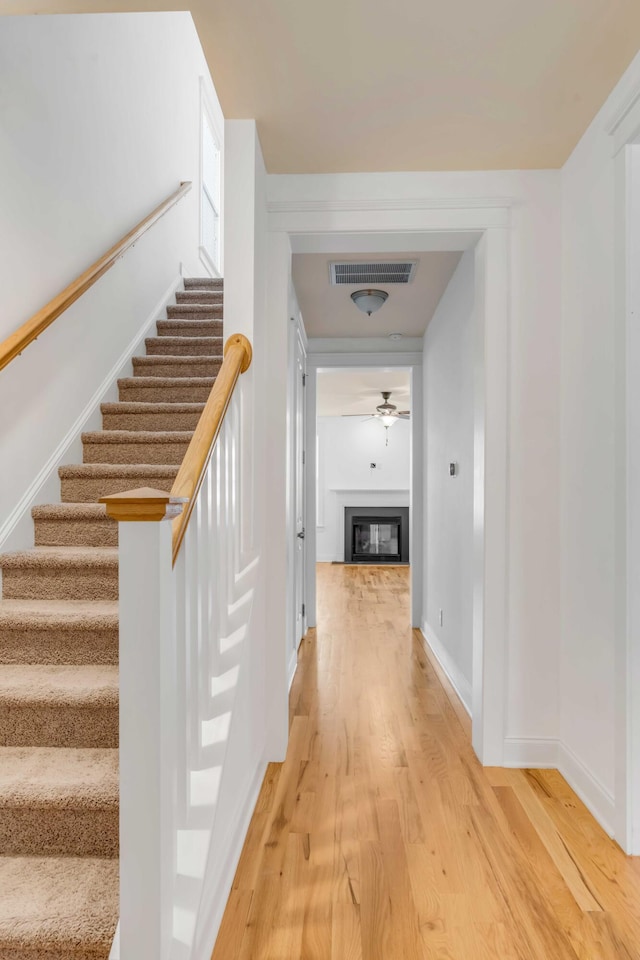 stairs with a ceiling fan, wood finished floors, visible vents, baseboards, and a glass covered fireplace