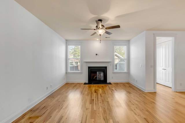 unfurnished living room with a fireplace with flush hearth, light wood-style floors, baseboards, and a healthy amount of sunlight