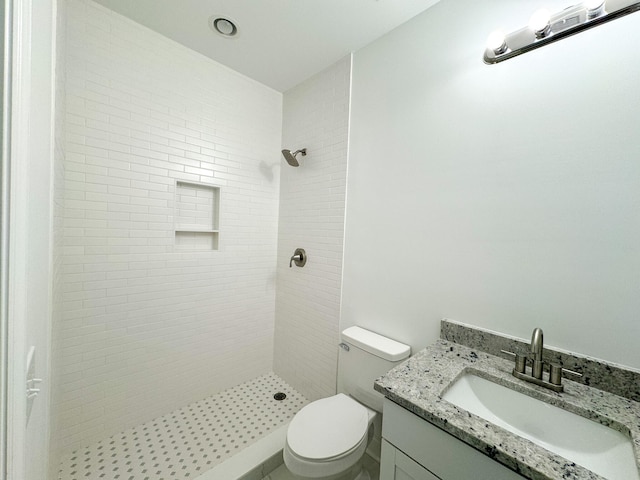 bathroom featuring toilet, a tile shower, and vanity