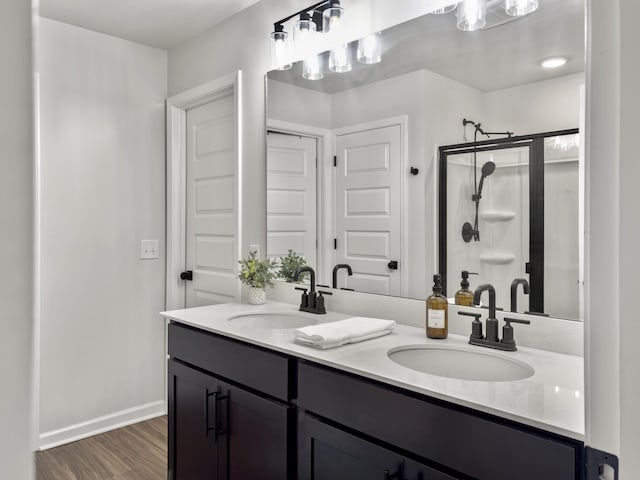 bathroom featuring wood finished floors, a sink, a stall shower, and double vanity