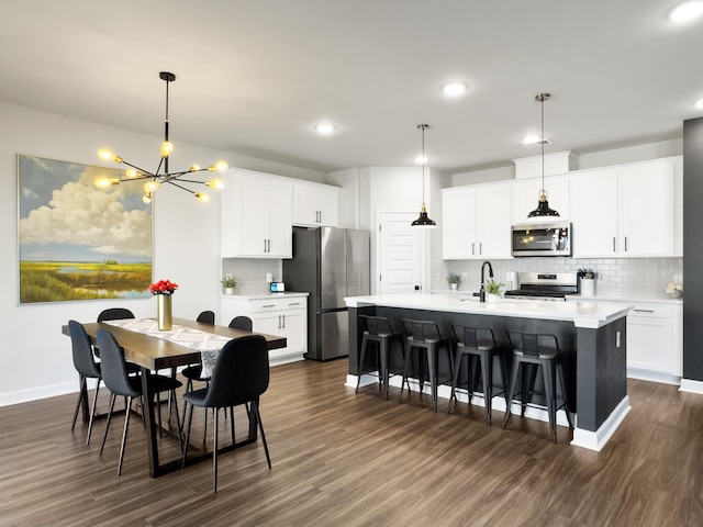 kitchen featuring a kitchen island with sink, tasteful backsplash, dark wood-style floors, a chandelier, and stainless steel appliances