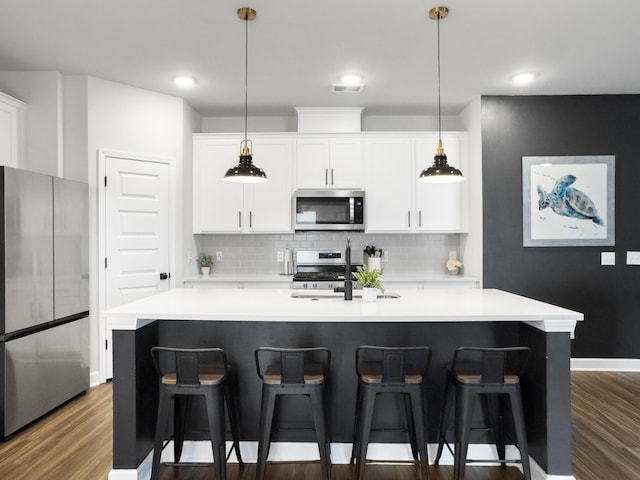 kitchen featuring an island with sink, light countertops, appliances with stainless steel finishes, and dark wood-style floors