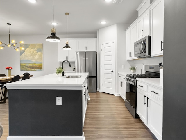 kitchen featuring appliances with stainless steel finishes, a sink, a kitchen island with sink, light wood-type flooring, and pendant lighting