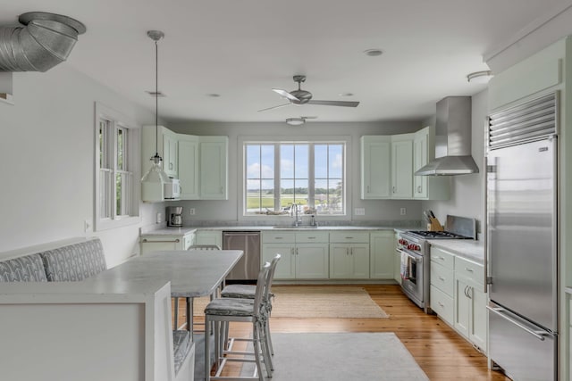 kitchen with wall chimney exhaust hood, sink, pendant lighting, high quality appliances, and a breakfast bar area