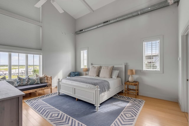 bedroom featuring multiple windows, ceiling fan, a towering ceiling, and light wood-type flooring