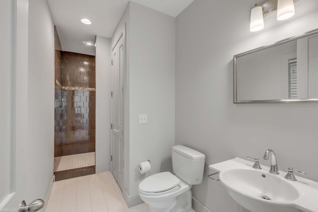 bathroom featuring tiled shower, toilet, and sink