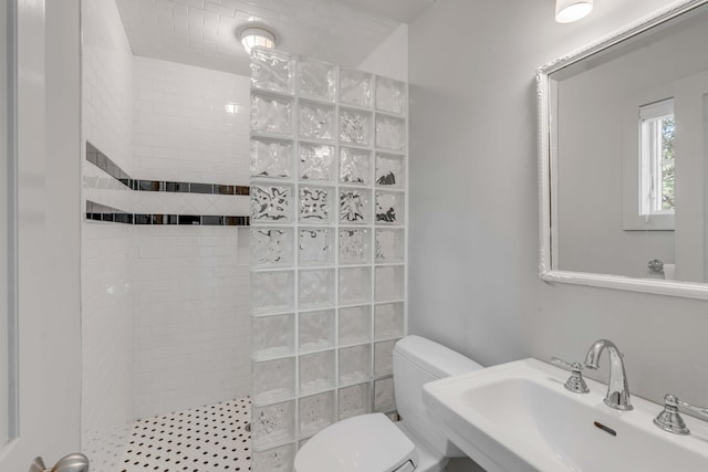 bathroom featuring toilet, a tile shower, and sink