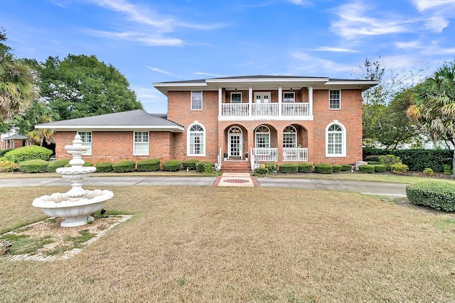 view of front facade with a balcony, brick siding, a porch, and a front yard