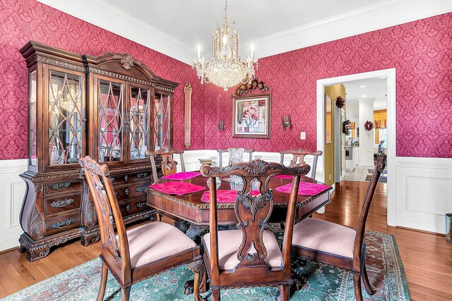 dining room with an inviting chandelier, wallpapered walls, wood finished floors, and wainscoting