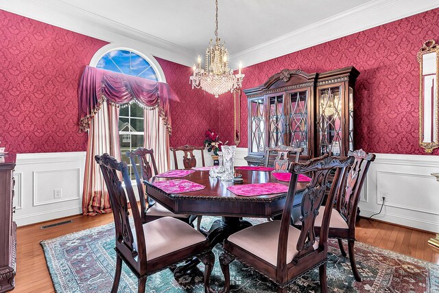 dining area featuring wainscoting, ornamental molding, a chandelier, wallpapered walls, and wood finished floors