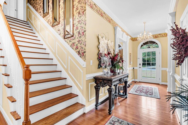 foyer with ornamental molding, stairway, a chandelier, and wood finished floors