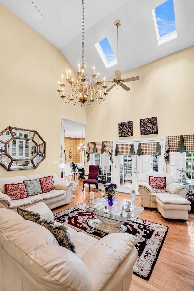 living room featuring ceiling fan with notable chandelier, a wealth of natural light, a skylight, and light wood-type flooring