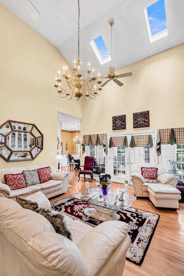 living room featuring ceiling fan with notable chandelier, high vaulted ceiling, wood finished floors, and a skylight