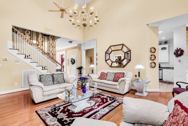 living room with light hardwood / wood-style flooring, a high ceiling, and ceiling fan with notable chandelier