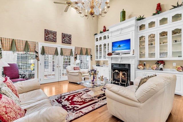 living room with ceiling fan with notable chandelier, light hardwood / wood-style floors, a towering ceiling, and a premium fireplace