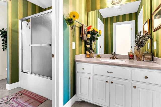 full bathroom with combined bath / shower with glass door, wallpapered walls, tile patterned flooring, and vanity