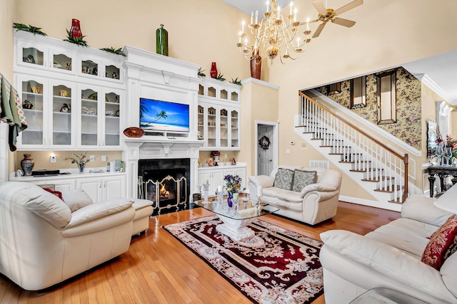living room featuring stairway, a premium fireplace, wood-type flooring, a towering ceiling, and an inviting chandelier