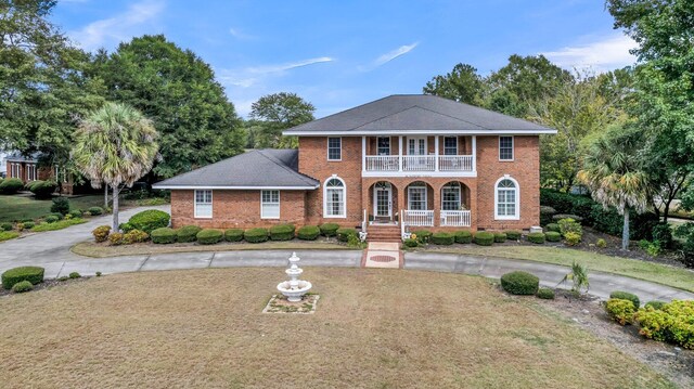 view of front of home featuring a front yard, curved driveway, brick siding, a balcony, and a porch