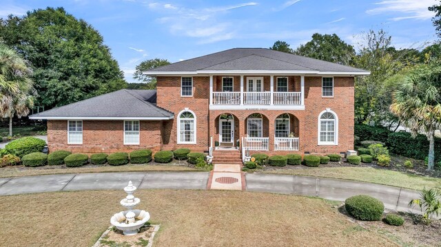 view of front facade with a balcony, covered porch, brick siding, and a front yard