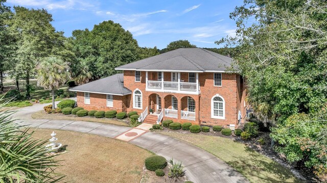 view of front of home featuring covered porch, a balcony, brick siding, and curved driveway