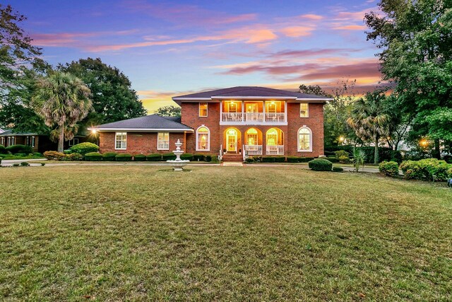 view of front facade featuring a porch, a balcony, brick siding, and a front lawn