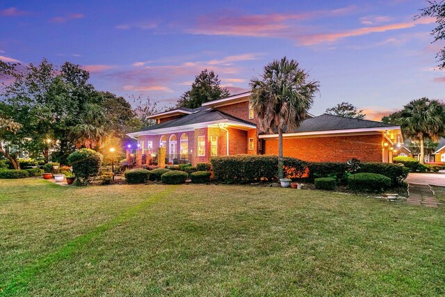 back of property at dusk with brick siding and a yard
