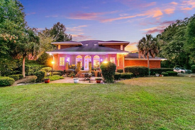 back of house at dusk with a yard and a patio area