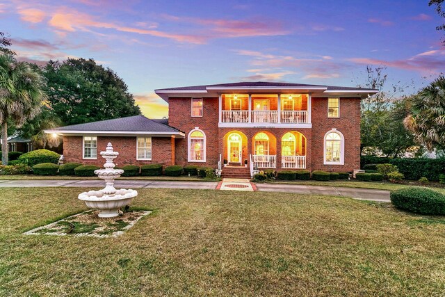 view of front facade with a balcony, brick siding, a porch, and a yard