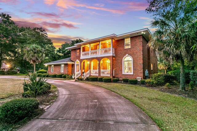 view of front of property with a balcony, a front yard, brick siding, curved driveway, and a porch