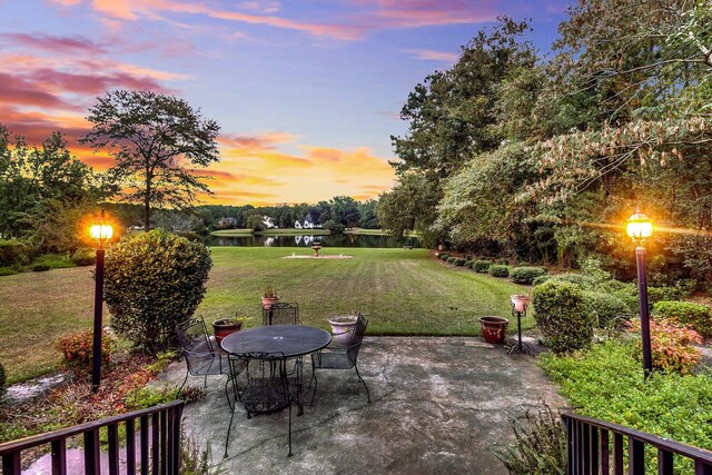 patio terrace at dusk with a water view and a yard