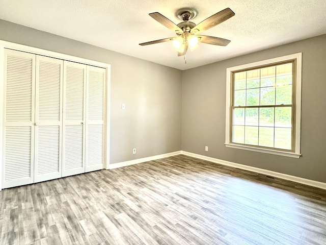 unfurnished bedroom featuring wood finished floors, baseboards, a closet, a ceiling fan, and a textured ceiling