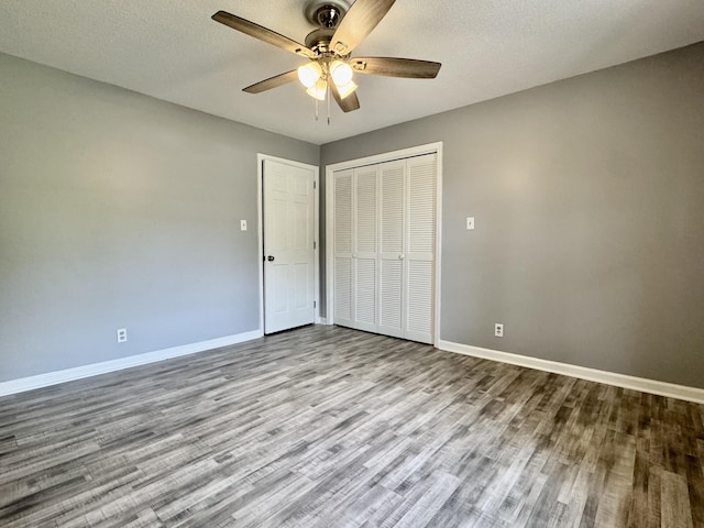 unfurnished bedroom featuring wood finished floors, baseboards, a closet, ceiling fan, and a textured ceiling