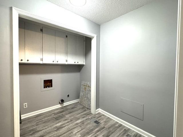 clothes washing area featuring cabinet space, electric dryer hookup, wood finished floors, hookup for a washing machine, and a textured ceiling